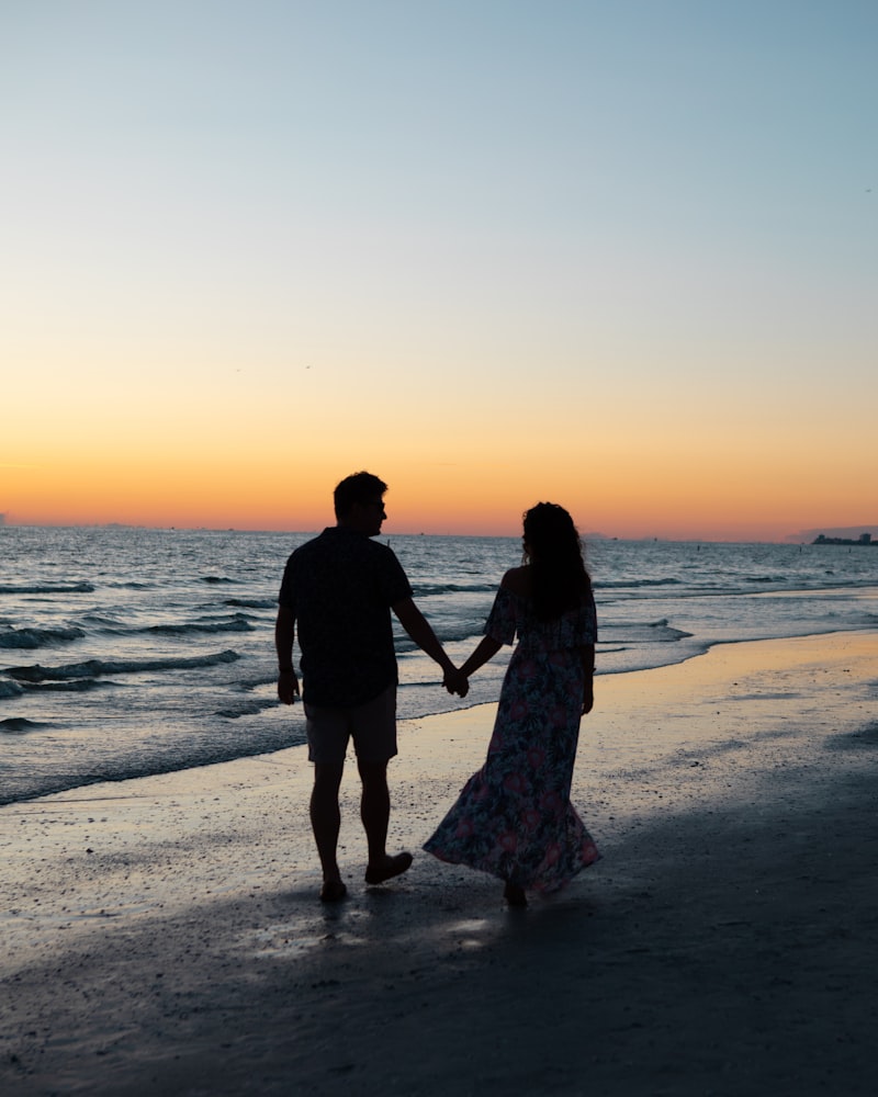 Pareja caminando de la mano por la orilla del mar al atardecer